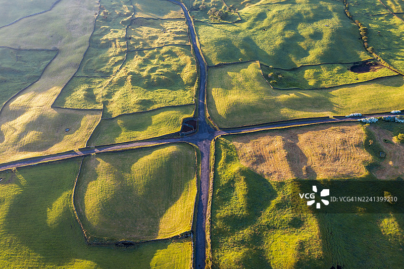宁静乡村风光中，拼凑的绿色田野和蜿蜒的道路的空中视角图片素材