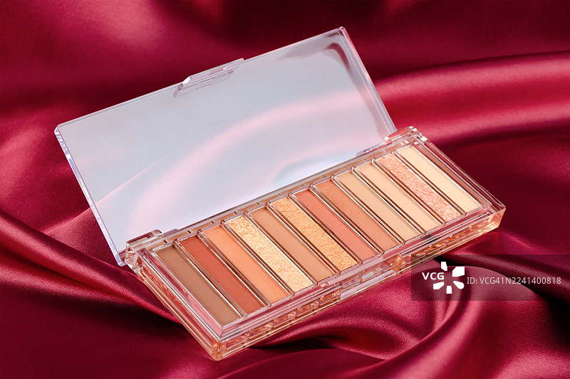 红色丝绸背景上的化妆品，眼影调色板。图片素材