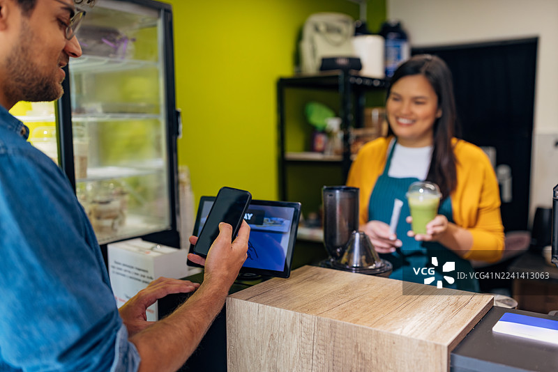 男顾客在取冰沙时，使用智能手机在自助服务终端付款图片素材