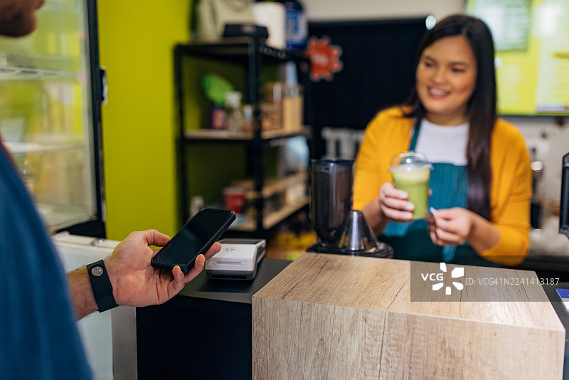 一位友好的女售货员递给男士一杯他订购的健康冰沙，他前来取货。图片素材