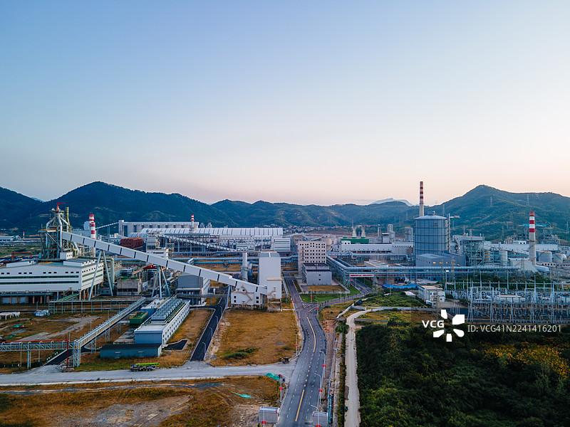 夕阳下的工业工厂景观，包括传送带、发电厂结构、石材加工设施和机械，在温暖的橙色天空下，凸显工业生产和能源基础设施。图片素材