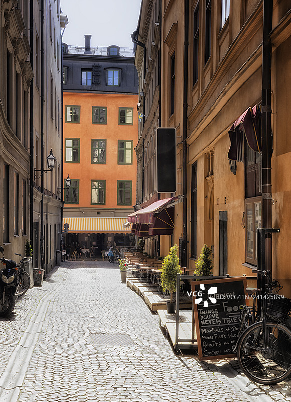 斯德哥尔摩老城(Gamla Stan)的广告牌,展示典型的瑞典美食,背景是中世纪橙色石砌建筑、户外咖啡馆和夏日阳光。图片素材