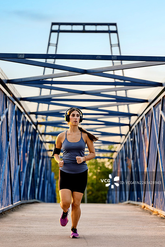 日落时分，一名戴着耳机的运动员正在城市桥梁上奔跑。图片素材