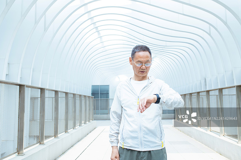 一位亚洲老年男子在公园里查看智能手表上的信息图片素材