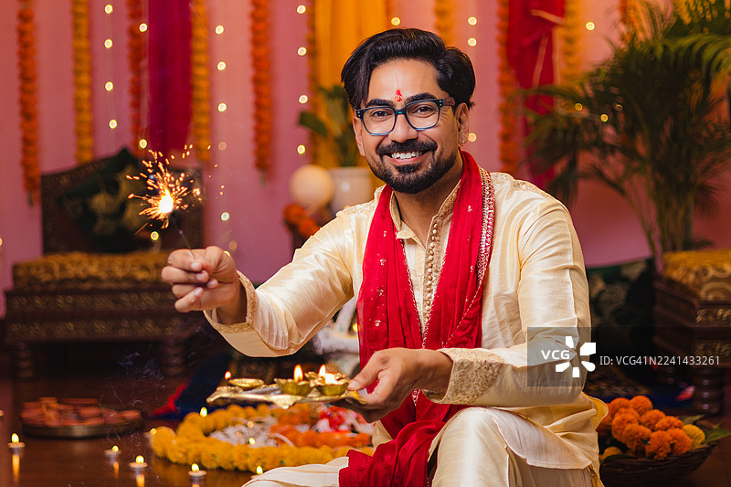 印裔男子在家里手持仙女棒和油灯庆祝排灯节——节日传统肖像图片素材
