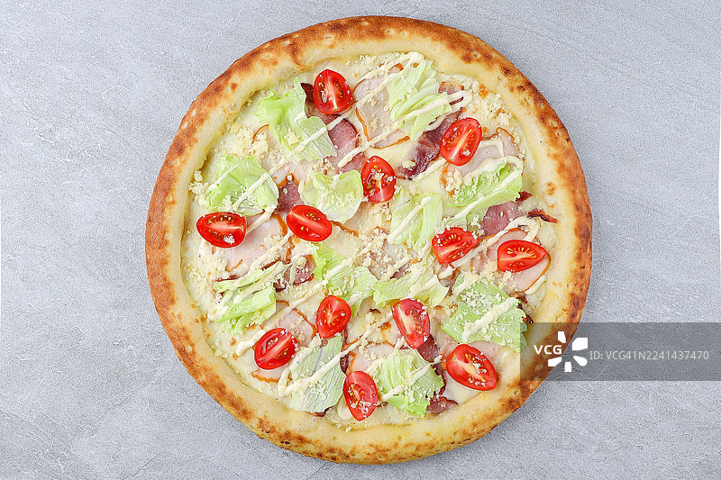 上面是美味的披萨，配有新鲜的食材，包括番茄、生菜和蛋黄酱，在灰色背景上从正上方拍摄图片素材