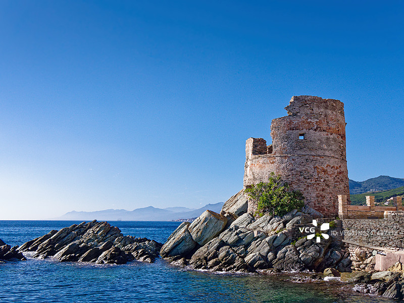 古老的石塔遗址矗立在岩石海岸上，蔚蓝的大海和远山在明媚的天空下，法国，科西嘉岛图片素材