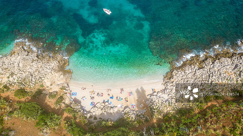 从空中俯瞰，一片僻静的白色沙滩，碧绿的海水，人们在阳光下悠闲放松，附近有一艘船在航行图片素材