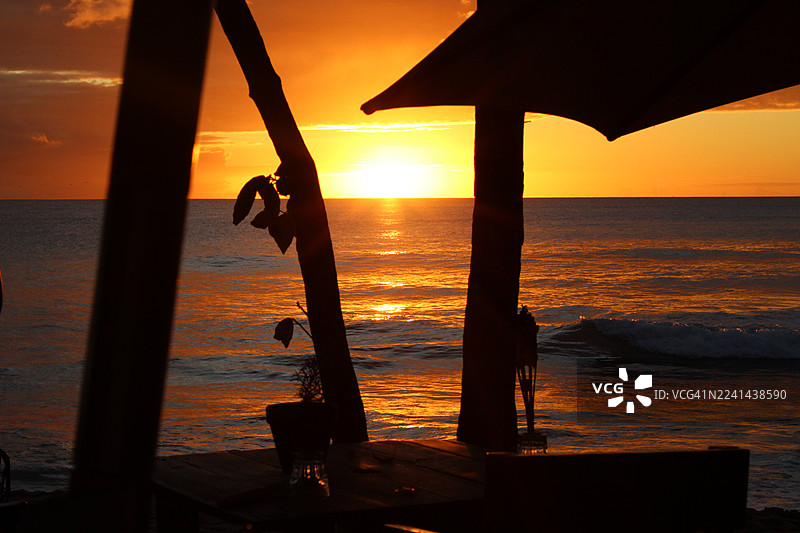 前景是海滩咖啡馆的剪影，背景是戏剧性的海边日落图片素材