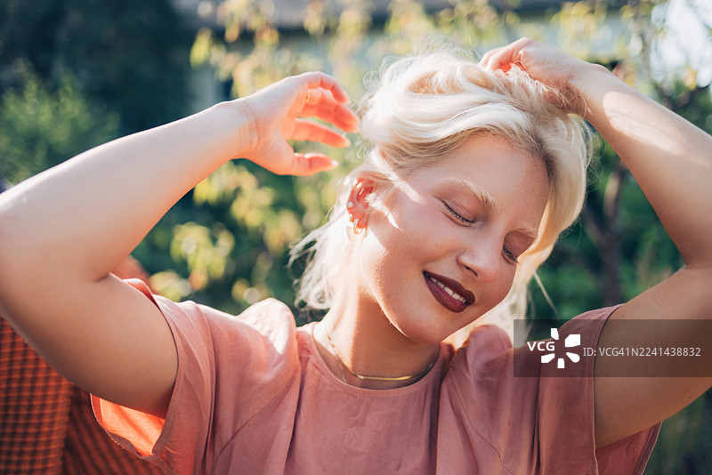 快乐的金发女子穿着粉色上衣在户外享受阳光明媚的时刻，放松的肖像图片素材