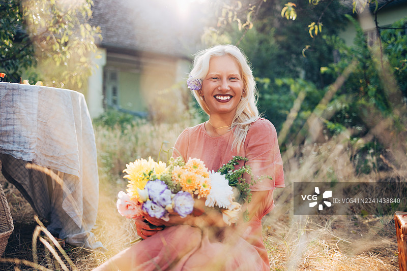阳光明媚的夏日，一位女士在户外手持色彩缤纷的鲜花束，充满了夏日的温暖气息。图片素材