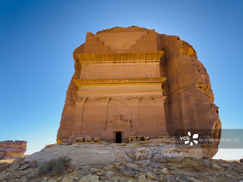 沙特阿拉伯乌拉古城，一块刻有古代纳巴泰墓穴建筑的岩石，背景是湛蓝的天空图片素材