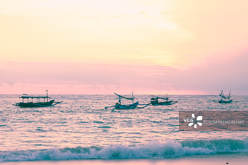 日落时分，传统渔船漂浮在平静的海面上，柔和的粉彩色调渲染着天空，温柔的海浪拍打着海岸。图片素材