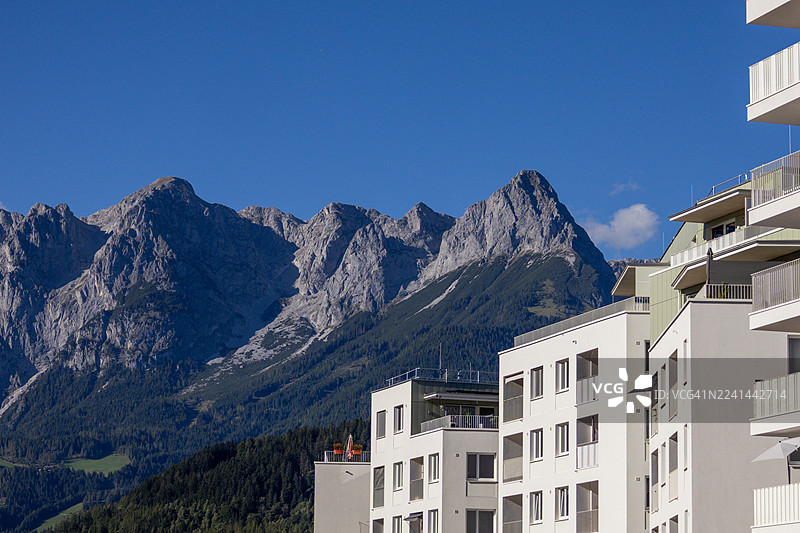 带有阳台的现代住宅楼，背景是雄伟的山脉和湛蓝的天空。图片素材
