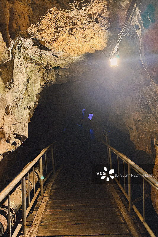 灯火通明的木制人行桥通往一个有崎岖岩石构造的黑暗洞穴图片素材