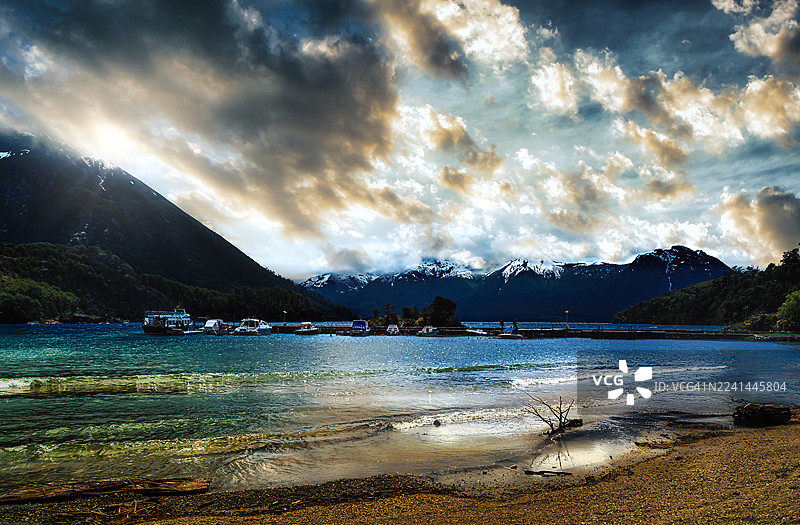 阿根廷圣卡洛斯-德巴里洛切，群山、船只和沙滩环绕的宁静湖泊上的戏剧性日落图片素材