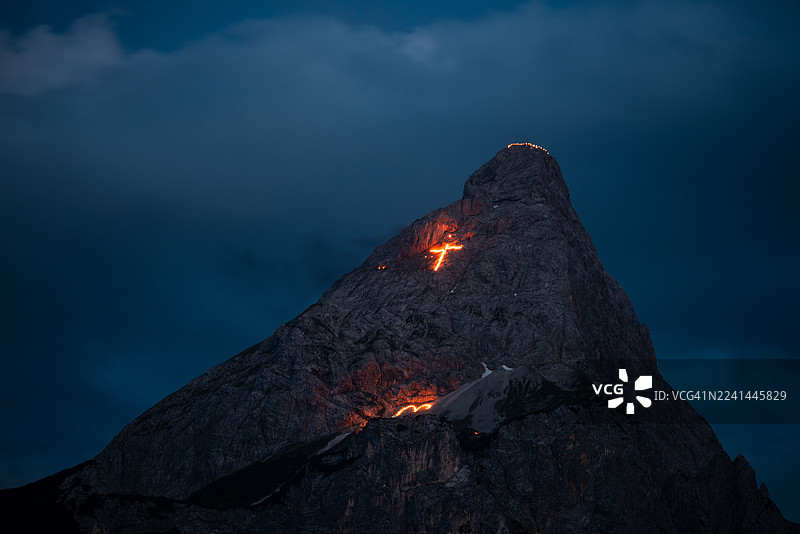 夜晚的山上，闪耀着基督十字架和象征信仰与传统的符号，奥地利埃尔瓦尔德。图片素材