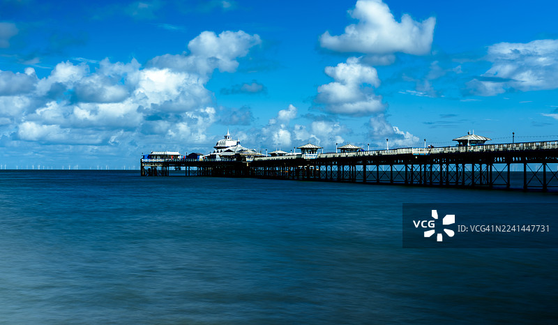 英国兰迪德诺，平静湛蓝的海面上延伸的长长的码头，天空充满活力，点缀着零散的云朵，风景优美。图片素材
