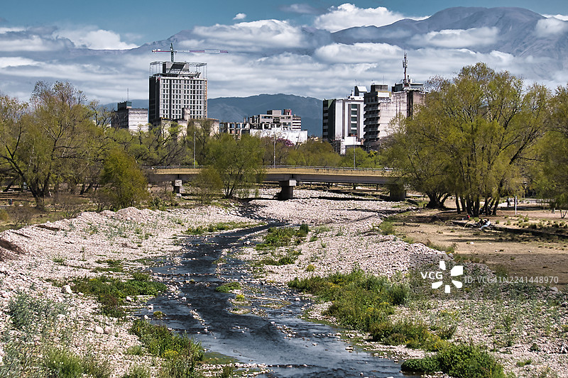 阴天下的城市景观，有河床和现代建筑，点缀着郁郁葱葱的绿树图片素材