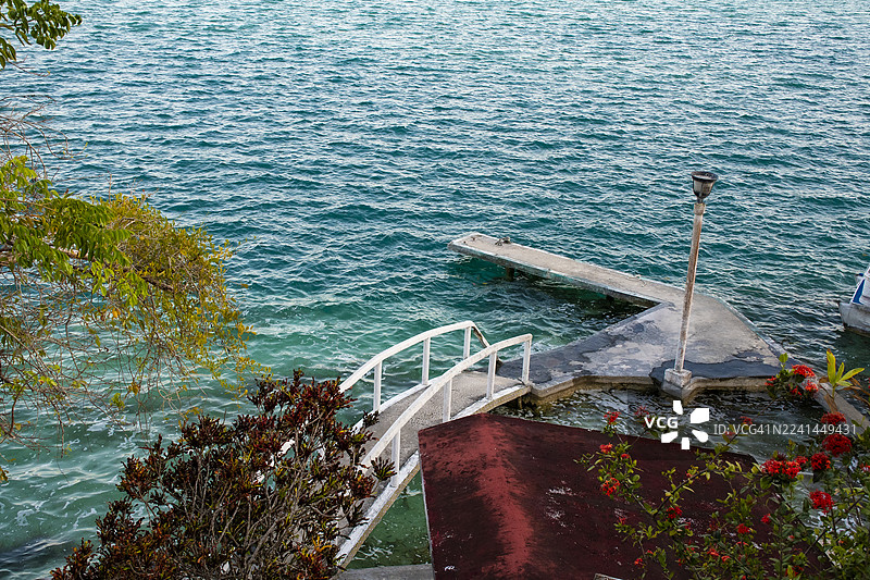 从高处俯瞰宁静的蓝色大海，一座混凝土码头和茂密的绿色植物构成了画面的框架，墨西哥，巴卡拉尔图片素材