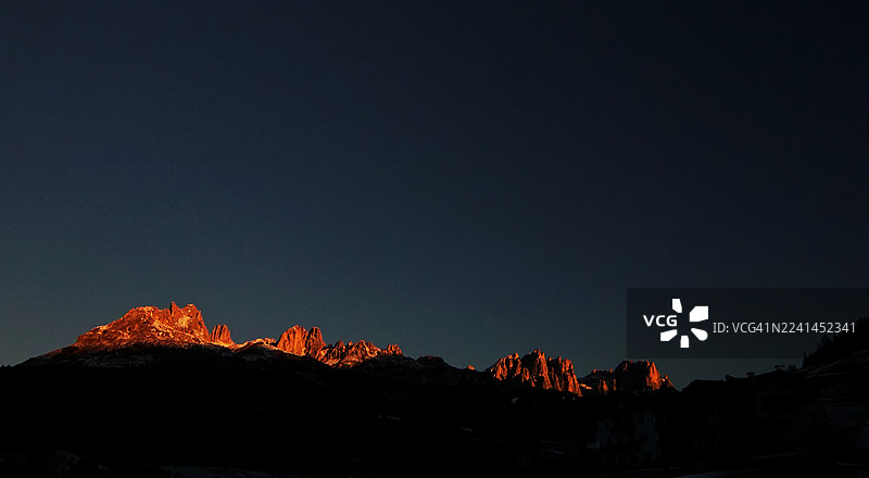 意大利圣佩莱格里诺泰尔梅，山峰剪影在黑暗清澈的夜空中，温暖的光线照亮山顶，戏剧性的低角度视角图片素材