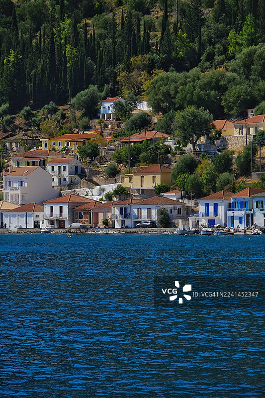 希腊伊萨基岛风景如画的海岸村庄，传统建筑依山而建，俯瞰着湛蓝的大海，天空晴朗。图片素材