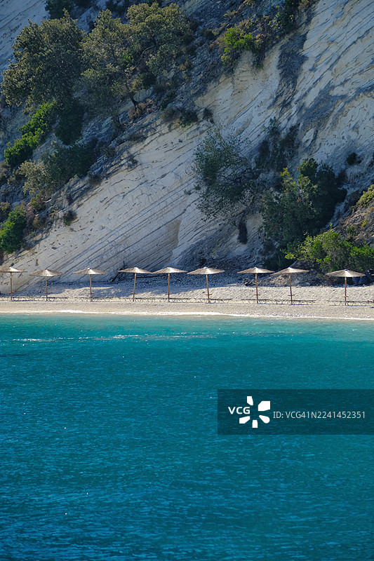 爱琴海海边，希腊斯卡拉，宁静的鹅卵石海滩，白色悬崖下的草伞，碧绿的海水图片素材