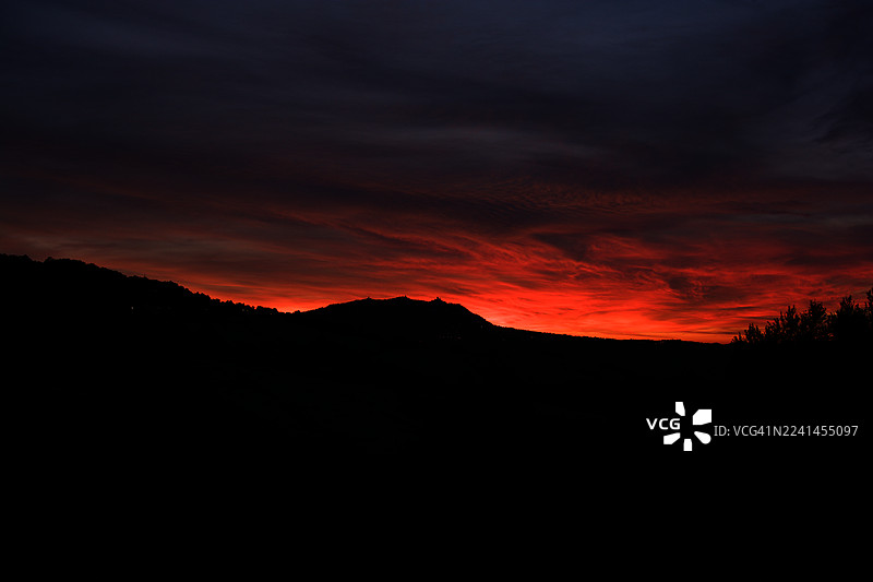 圣马力诺，剪影般群山与树木映衬下的戏剧性红色日落天空图片素材