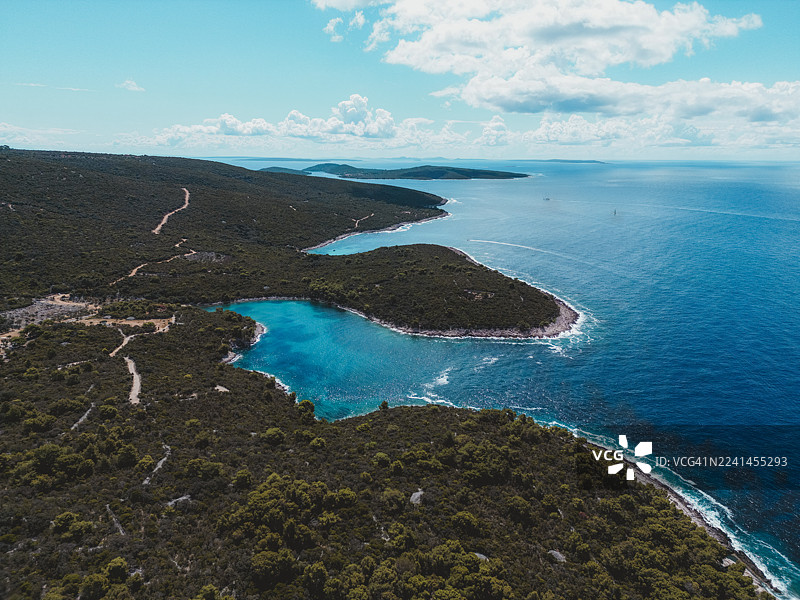 在晴朗有分散云层的天空下，克罗地亚碧蓝的大海与郁郁葱葱的绿色海岸线交汇的令人惊叹的航拍景象图片素材