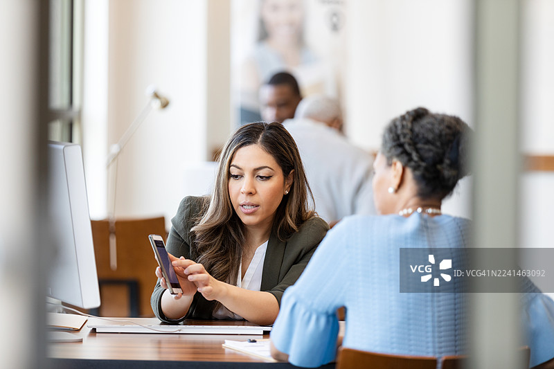 两位职业女性专注于交流手机技术。图片素材