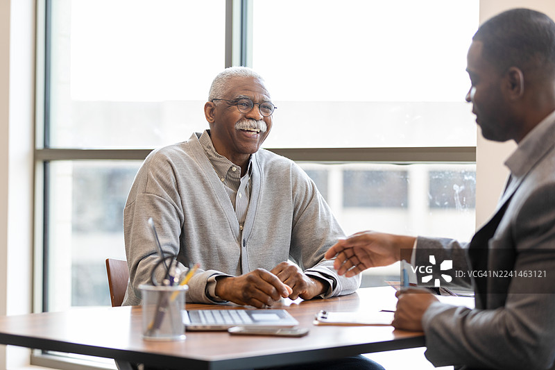 年长的男士在办公室里与年轻的专业人士交流，面带微笑。图片素材