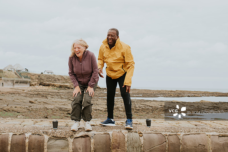 一对年长的夫妇站在码头上，笑得弯下了腰，妻子笑得前仰后合，丈夫在她身边得意地咯咯笑。图片素材