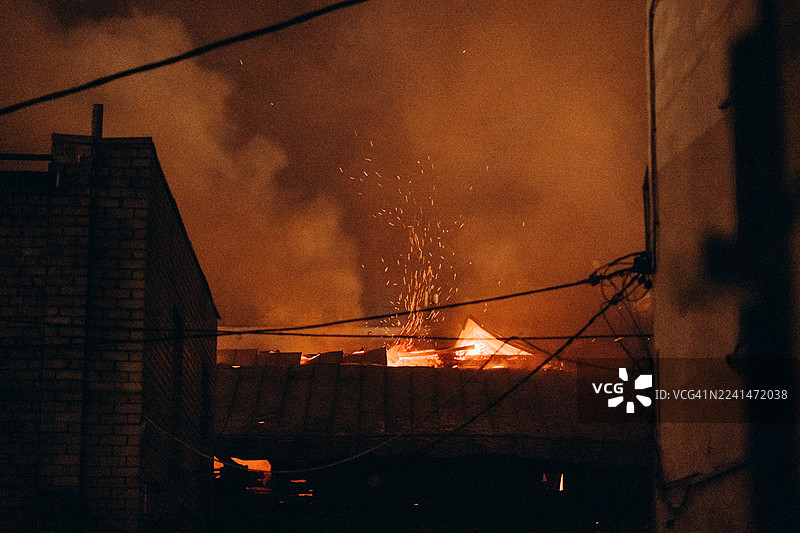 夜间，房屋屋顶燃起熊熊大火，火星四溅。图片素材