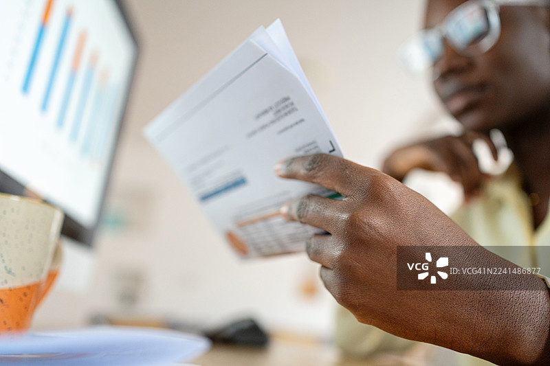 一位年轻的黑人女性在她的办公桌前审阅财务报表，电脑屏幕上显示着图表。图片素材