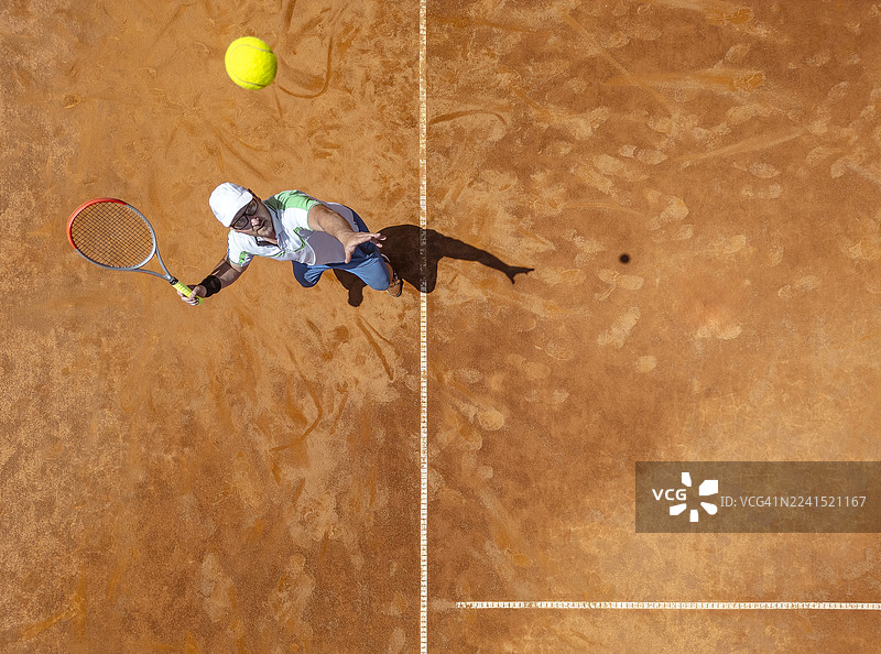 网球运动员在红土场上发球的航拍图，身穿白色运动服图片素材