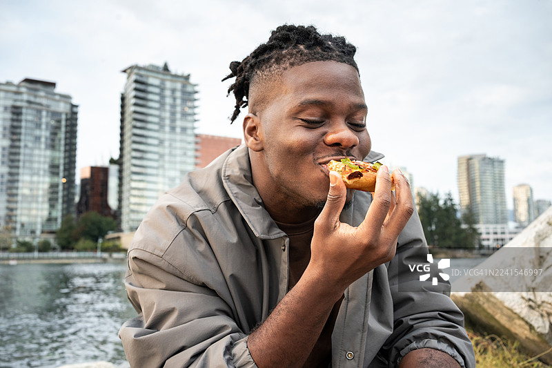 年轻的非裔美国男子在户外享用美味的披萨，背景是城市景观。图片素材