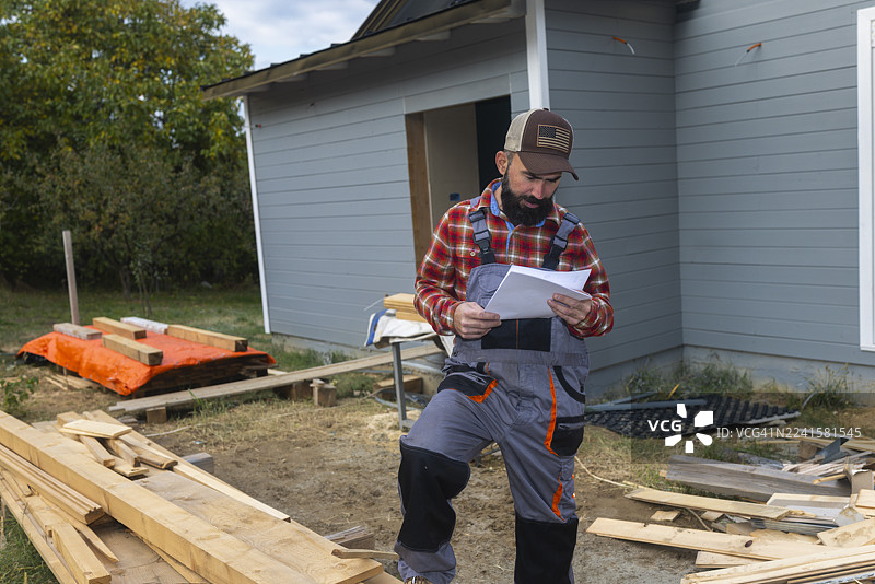 留着胡子的男建筑工穿着格子衬衫在户外建筑工地建造木屋图片素材