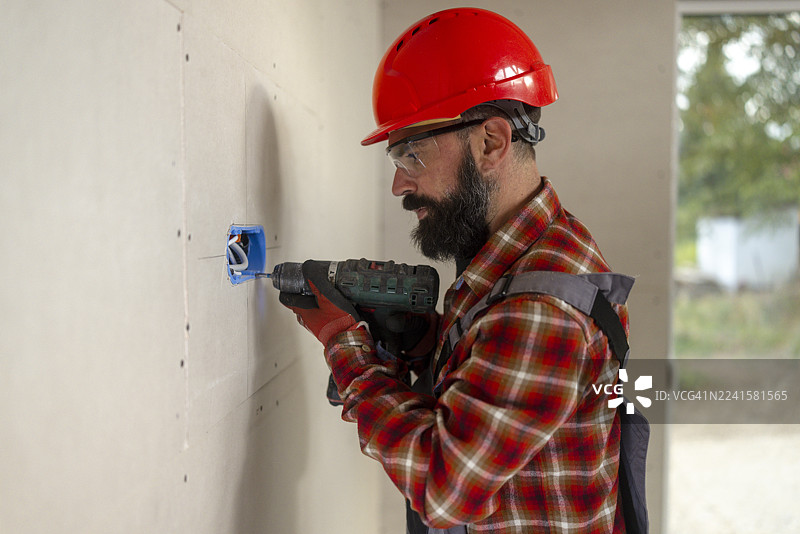 装修中的木屋里，留胡子的男性建筑工人正在用电钻安装电源插座图片素材