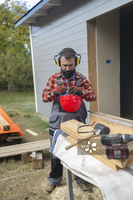 胡须男工人正在户外为施工中的木屋准备安全头盔图片素材