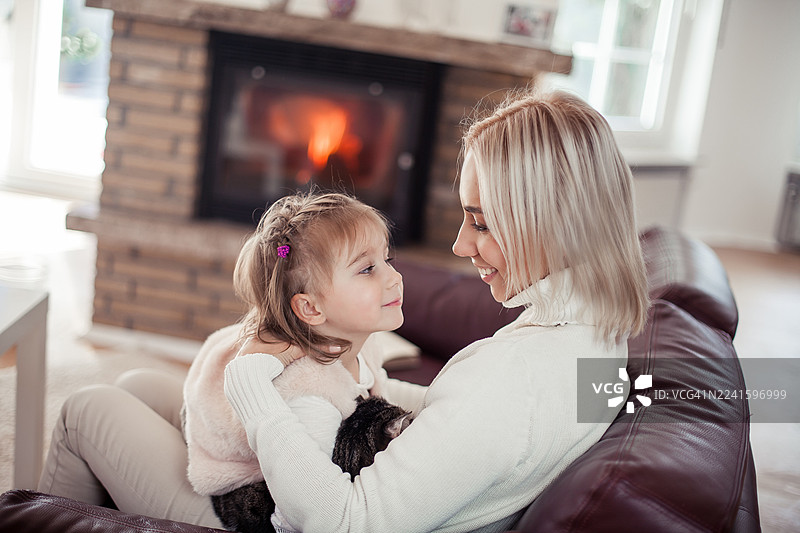 漂亮的妈妈、小女儿和一只猫坐在壁炉旁的沙发上。居家室内环境，温馨舒适。图片素材