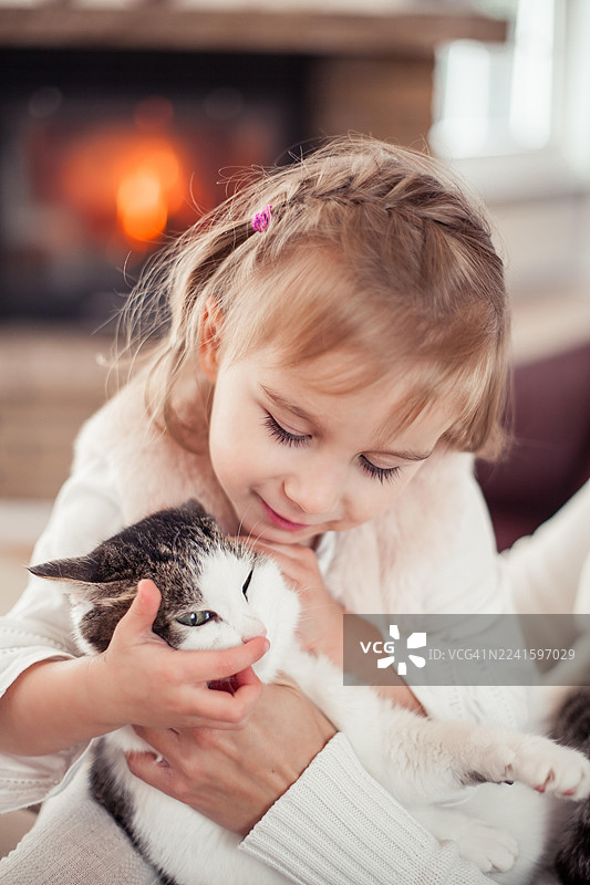 可爱的小女孩抱着猫，坐在壁炉旁。温馨的家。图片素材