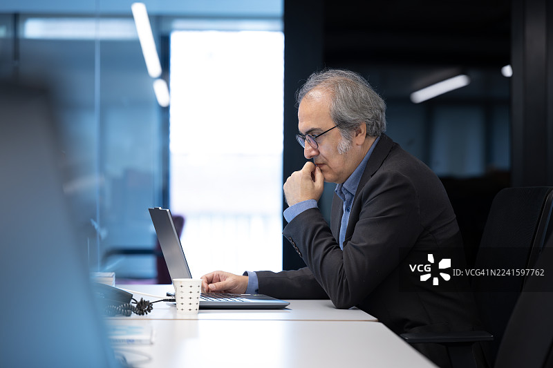 商务人士在办公室用笔记本电脑工作时思考图片素材