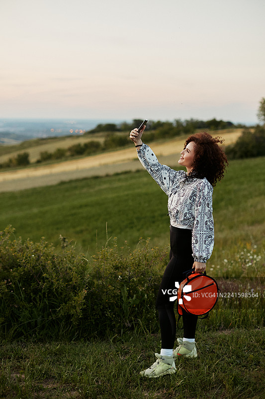 一名女子背着红色背包在山坡上自拍图片素材