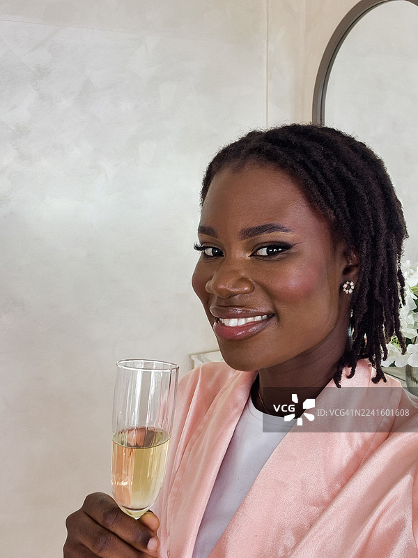 一位年轻的黑人女性在美容院化完妆后，一边喝着香槟一边自拍。图片素材