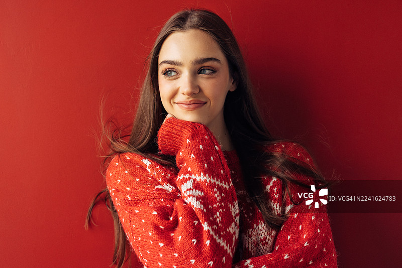 身穿红色针织毛衣的女子在红色背景前温柔微笑，一幅舒适喜庆的肖像照图片素材