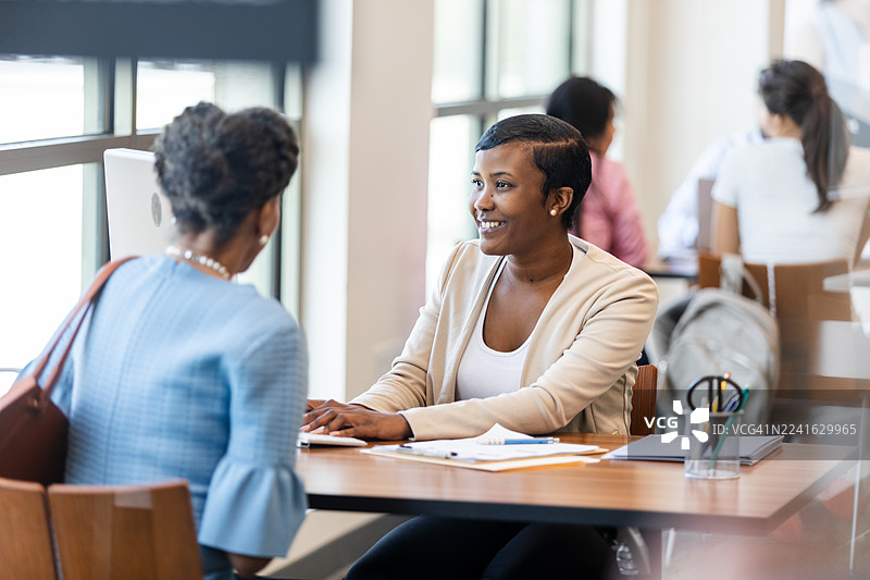 两位女性在木桌旁协作，交流想法并进行积极沟通。图片素材