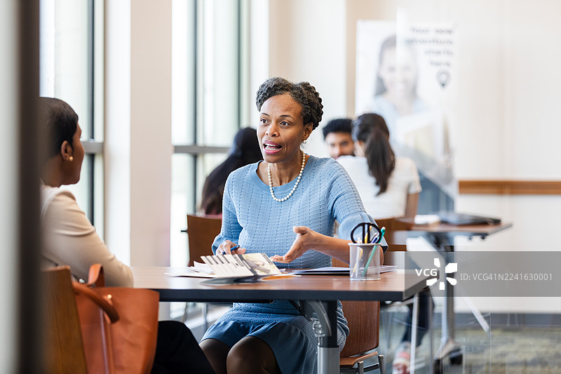 一位成熟的女性在明亮现代的办公室环境中，热情地向同事解释某事。图片素材