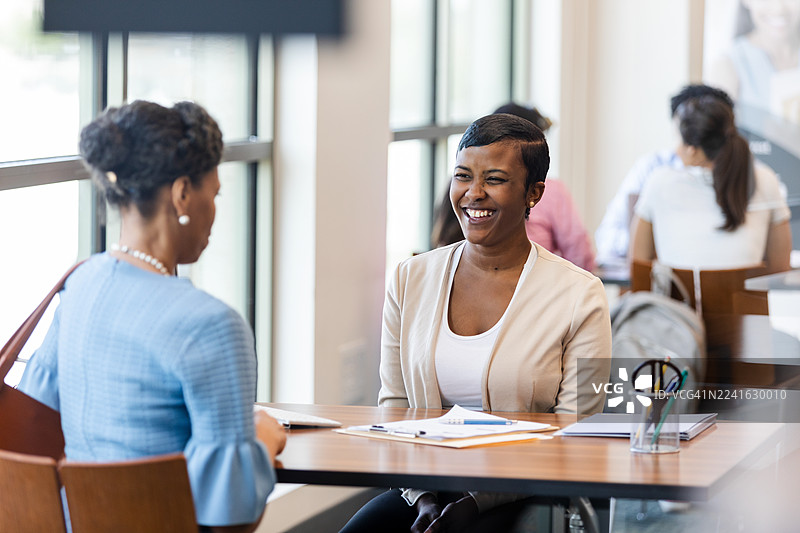 两位女士在室内交谈，她们面带微笑，看起来像是在合作。图片素材