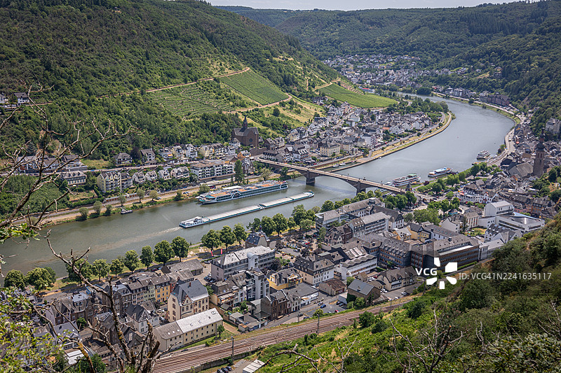 高角度拍摄的风景如画的小镇，坐落于山谷中，一条河流蜿蜒穿过，四周环绕着郁郁葱葱的绿色山丘。图片素材