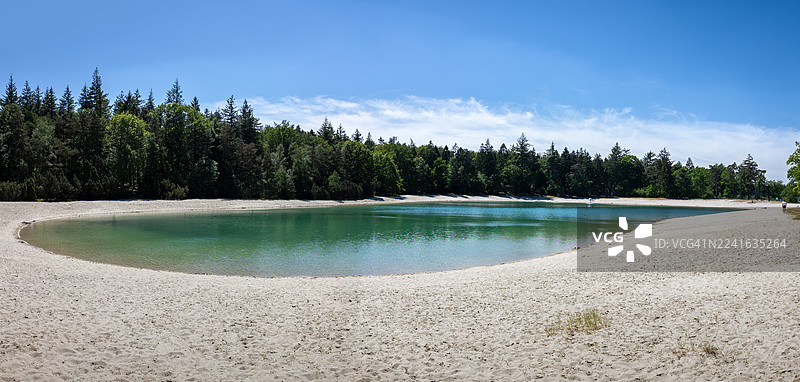 开阔的湖泊全景，湖边有沙滩和茂密的森林，天空湛蓝图片素材